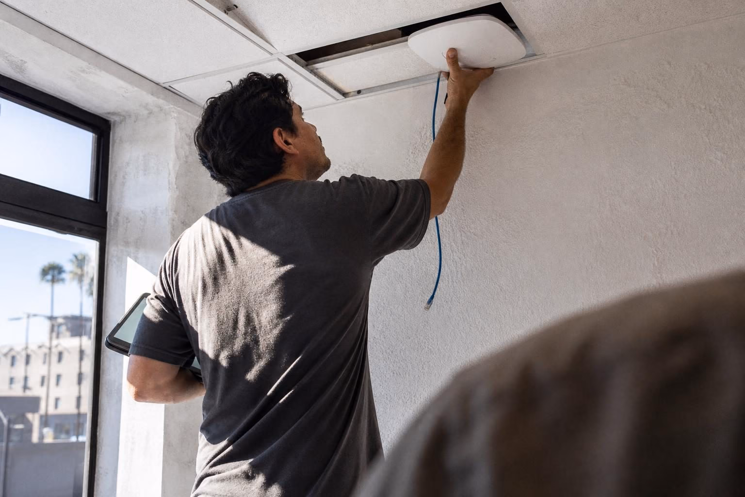 Technician mounting a ceiling wireless access point from a step ladder