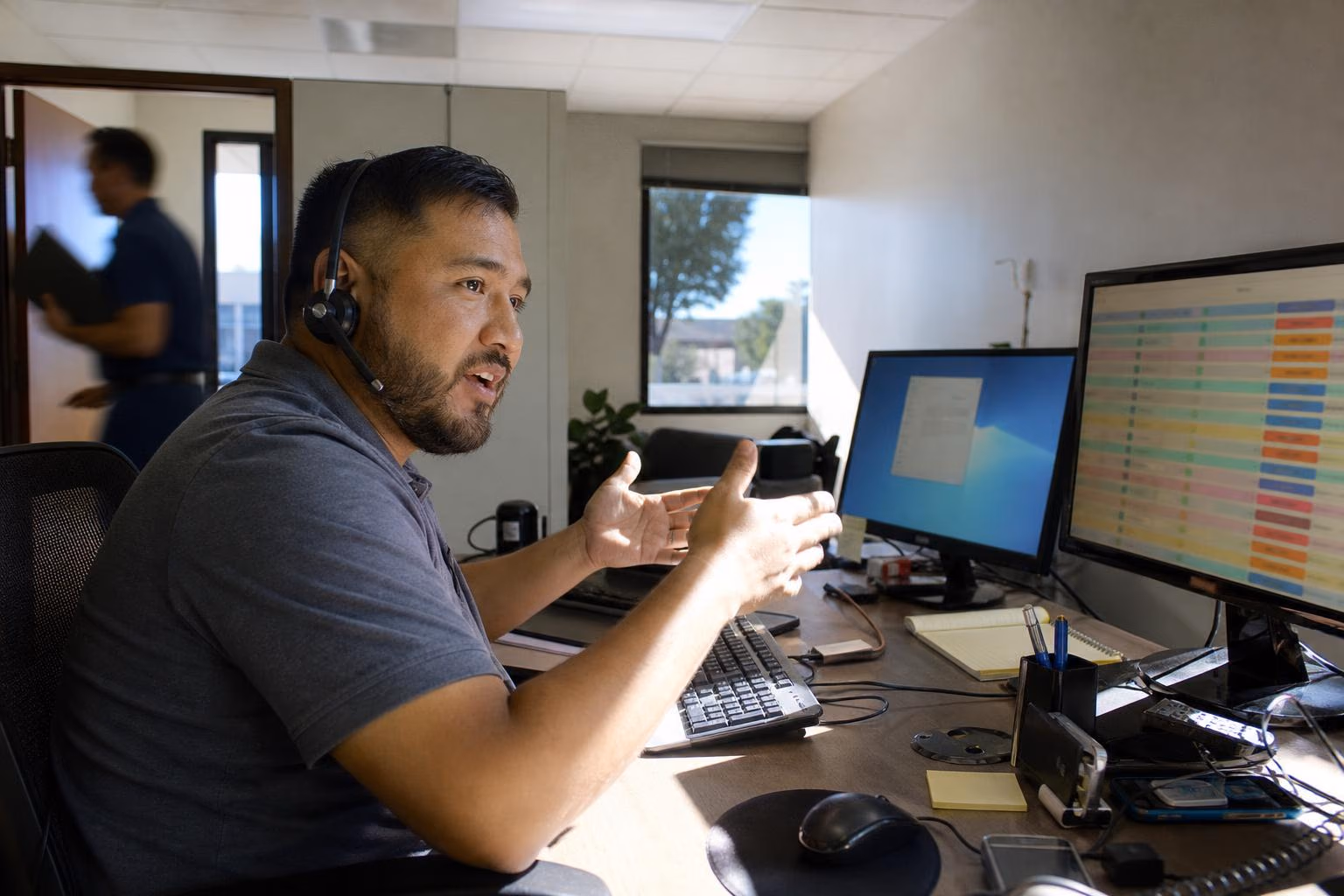Helpdesk technician on a headset beside a monitor of support tickets